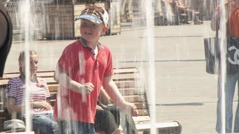 A boy in a baseball cap runs through the water jets of the fountain. bare feet Vídeo Stock 139440721