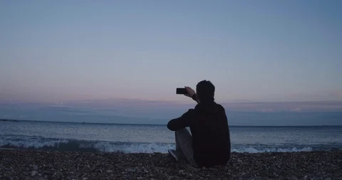 Boy on the beach during a sunset taking a selfie Stock Footage 125945176