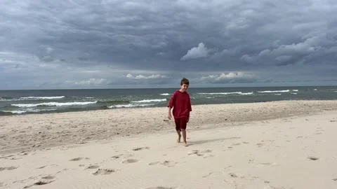 A boy on a beach under a dramatic sky, showing calm and freedom in a setting Stock Footage 279184302