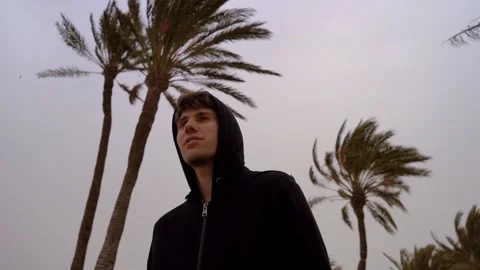 Boy in a beach whit a palm trees moving by the wind behind him Stock Footage 148500482