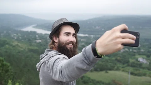 A boy with a beard and hat takes a selfie in a nice place Stock Footage 127184048