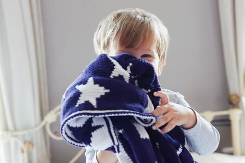Boy on bed hiding behind navy blue star patterned woollen blanket Stock Photos