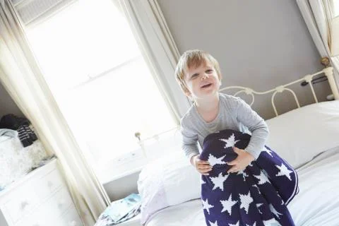 Boy on bed holding behind navy blue star patterned woollen blanket Stock Photos