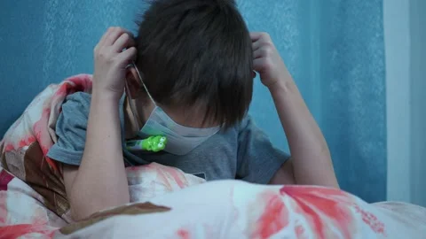 The boy on the bed measures the temperature with an electronic thermometer and Stock Footage 144262802