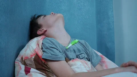 The boy on the bed measures the temperature with a thermometer, turns and smiles Stock Footage 144205588