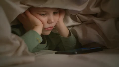 A boy in bed is watching something interesting on his phone. Stock Footage 260894608