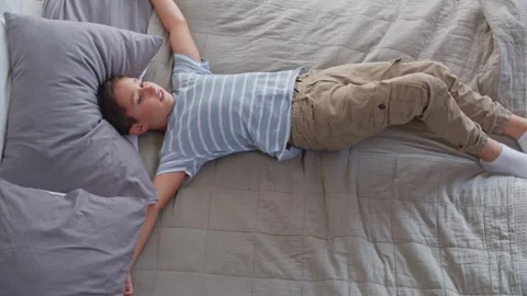 A boy in the bedroom imposingly jumps onto the bed, lies, stretches and yawns Stock Footage 255424345