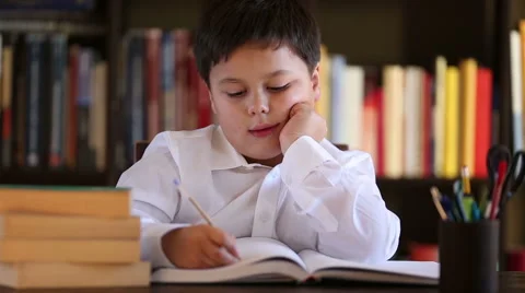 Boy behind desk writing, library in background Stock Footage 46316686