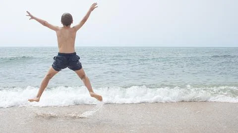 Boy from behind jumping for joy and from behind looking at the beach Foto stock