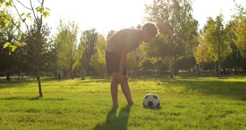 Boy bends over catching breath after soccer exercise in park at sunset. Child Stock Footage 346690562