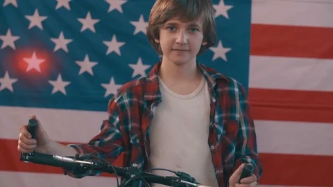 Boy with bicycle posing in front of american flag. shot in slow motion Stock Footage 75781630