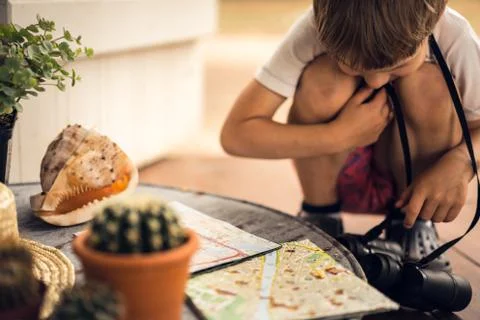 Boy with binoculars exploring the map on the table. Stock Photos