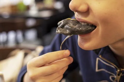 Boy bites a black dumpling from a fork. National food Stock Photos