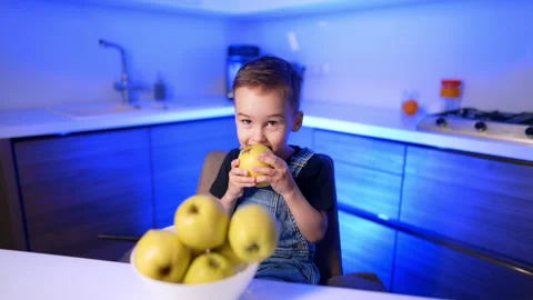 Boy biting into apple in blue lit kitchen Stock Footage 342160824