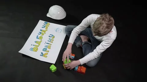 A boy on a black background sits in a construction helmet and plays constructor. Stock Footage 175996583