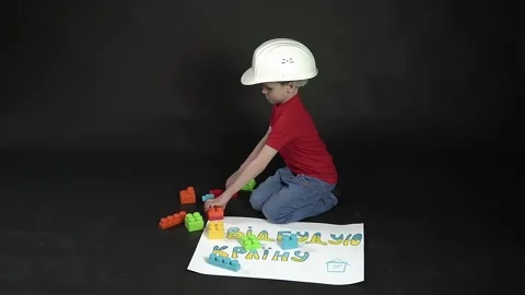A boy on a black background sits in a construction helmet and plays constructor. Stock Footage 175996923