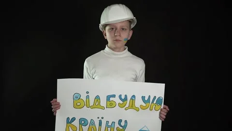 A boy on a black background stands in a construction helmet with a poster Stock Footage 175996344