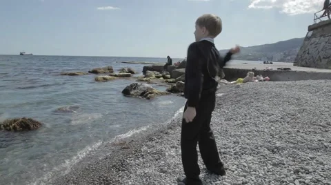 Boy in Black Clothes Squatting Throws Stones in a Sea on the Coast Stock Footage 62340540