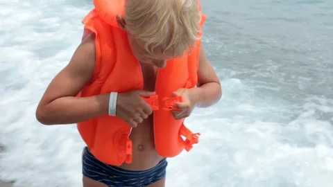 Boy blond, preschool age, buttoning orange inflatable vest Stock Footage 111668883