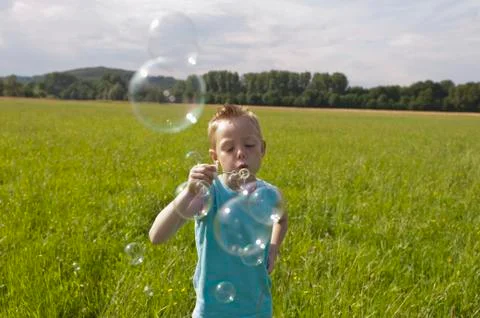 Boy blowing bubbles from bubble wand in meadow Stock Photos