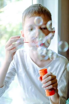 Boy blowing soap bubbles sitting on sofa at home. a lot of soap bubbles. Inte Stock Photos