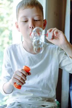 Boy blowing soap bubbles sitting on sofa at home. a lot of soap bubbles. Inte Stock Photos