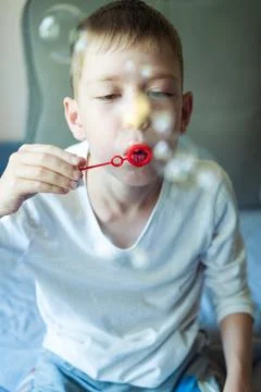 Boy blowing soap bubbles sitting on sofa at home. a lot of soap bubbles. Inte Stock Photos