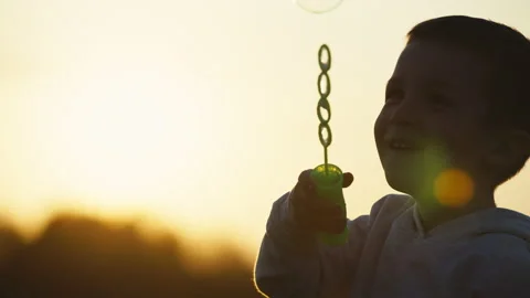 Boy blowing soap bubbles at sunset. The concept of a happy childhood, a cheerful Stock Footage 218254237