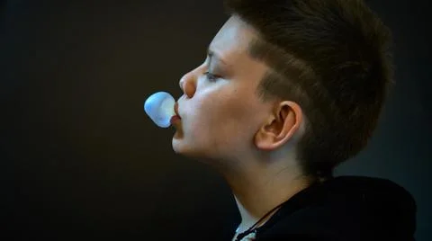 A boy blows bubbles out of chewing gum. The background is black Stock Photos