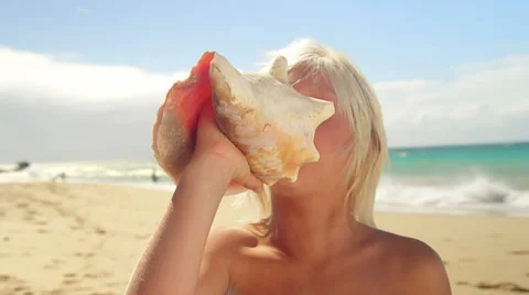 A boy blows into a conch shell while at the beach and smiles into the camera Stock Footage 33895420