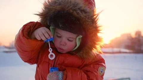 Boy blows soap bubbles in the Park with delight at winter sunset Vidéo 72705190