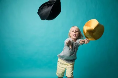 A boy on a blue background throws a yellow and black hat at the camera. Kids Stock Photos