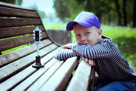 Boy in a blue cap sits at a bench with a traffic light Stock Photos