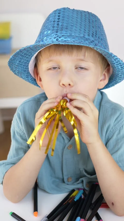 Boy in blue hat blows golden tinsel noisemaker with eyes closed in immersed 動画素材 345651794