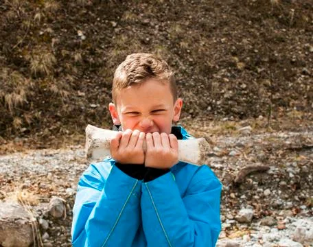 Boy in blue jacket bites into a very big old bone in a dried up river valley Stock Photos