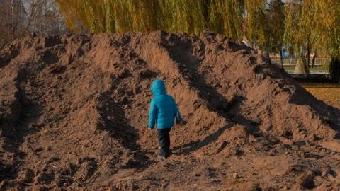 Boy in blue jacket, hat, boots and black pants climbs on foot a sand mountain. Stock Footage 169361840