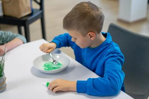 A boy in a blue jacket making green slime in a plate at the table Stock-Fotos