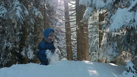 Boy in blue overalls on the hill playing snowballs in winter wood. Video stock 73174603