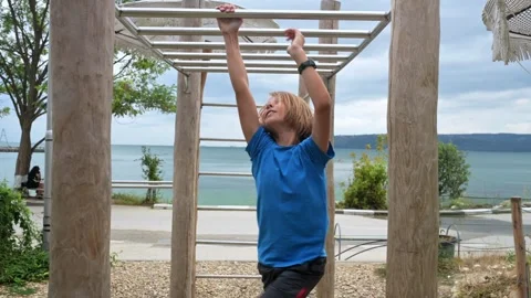 A boy in a blue shirt plays on a monkey bar near the seaside, enjoying an Stock Footage 283666764