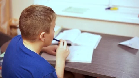 The boy is bored of sitting at the table and doing school tasks. Gnaws a ballpoi Stock Footage 99468187