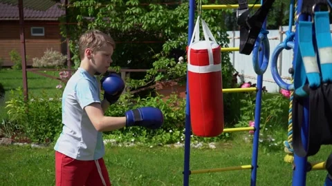 Boy in boxing gloves hitting a red punching bag Stockbeeldmateriaal 341360427