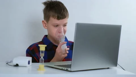 Boy is breathing in mask using nebulizer for inhalation at home watching laptop. Stock Footage 152716217