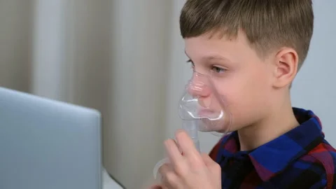 Boy is breathing in mask using nebulizer for inhalation at home watching laptop. Stock Footage 153767775