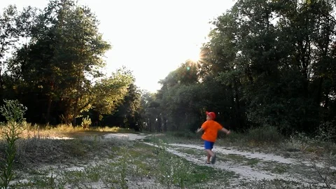 A boy in bright clothes runs along a forest path behind him a cyclist rides Stock Footage 103127372