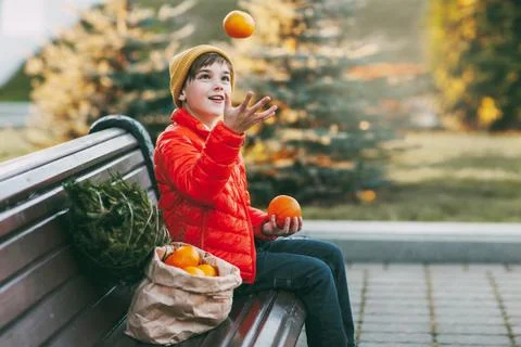 A boy in a bright orange jacket and a fashionable yellow hat sits on a bench Foto stock