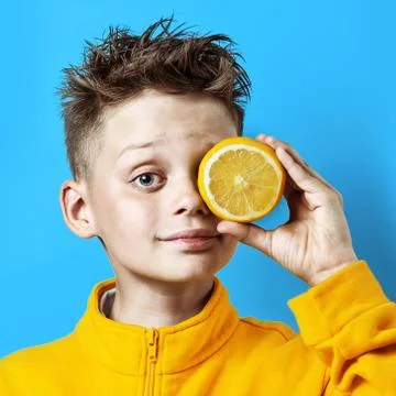 Boy in a bright yellow jacket with a lemon in his hand on a blue background Photos