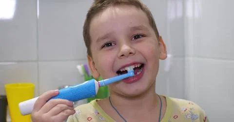 The boy brushes his teeth before going to bed with an electric toothbrush and Stock Photos