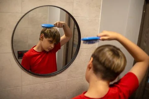 Boy Brushing Hair While Looking In Bathroom Mirror Stock Photos