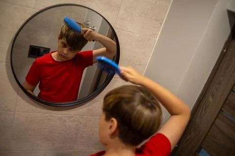 Boy Brushing Hair While Looking In Bathroom Mirror Stock Photos