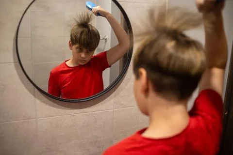 Boy Brushing Hair While Looking In Bathroom Mirror Stock Photos